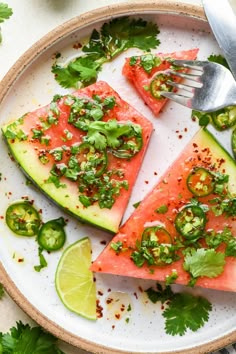 two slices of watermelon on a plate with limes and cilantro