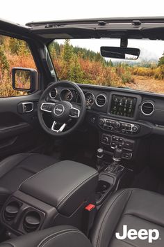 the interior of a jeep with black leather seats and steering wheel, in front of an open field