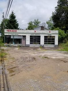 an abandoned gas station in the middle of a dirt lot with trees and bushes around it