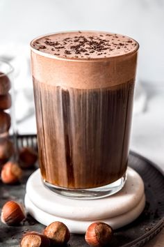 a glass filled with liquid sitting on top of a plate next to hazels and nuts