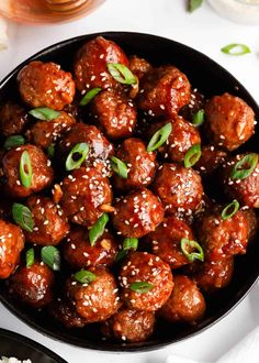 meatballs with sesame seeds and seasoning in a black bowl on a white table