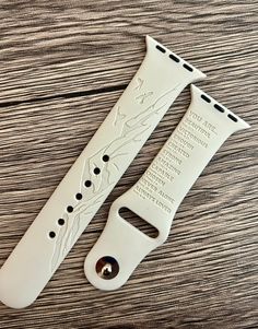 two white watch straps on top of a wooden table with words engraved on the strap