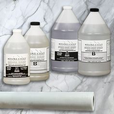 three bottles of liquid sitting on top of a white marble counter next to a roll of toilet paper