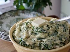 a bowl filled with spinach and cheese on top of a wooden table next to a potted plant