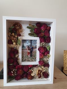 a photo frame with flowers and leaves in it on a table next to a vase