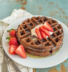 a waffle topped with syrup and strawberries on a plate next to a fork