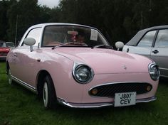 an old pink car is parked in the grass