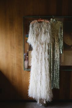 a white feather dress hanging on a wooden wall in front of a mirror and other items