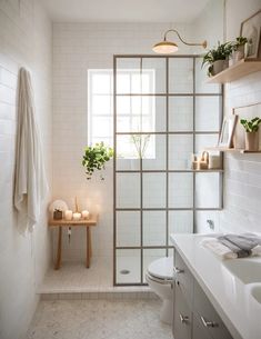 a bathroom with white tiles and plants on the shelves above the toilet, along with a shower stall