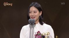 a woman standing at a podium with a microphone in front of her and holding an award