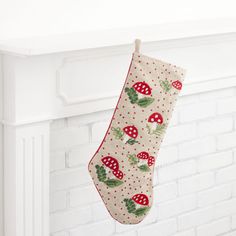 a christmas stocking hanging from a fireplace with red mushrooms and holly leaves on it