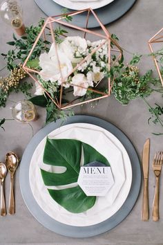 the table is set with plates, silverware and greenery