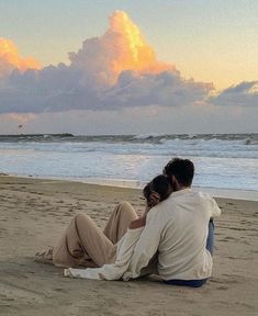 two people are sitting on the sand at the beach and watching the sun go down