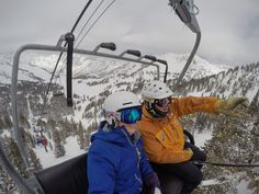 two people riding on a ski lift in the middle of snow covered mountains and trees