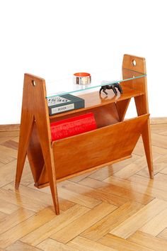 a wooden table with a glass top and books on it's legs, in the middle of a wood floor