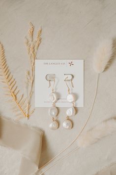 three pairs of earrings sitting on top of a white cloth next to some dried plants