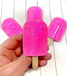 a hand holding a popsicle with pink decorations on it