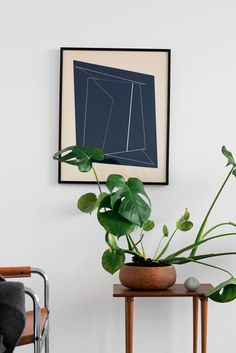 there is a potted plant sitting on a table in front of a framed art piece