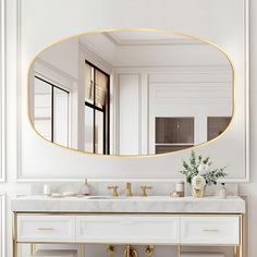 a white bathroom with gold accents and a large oval mirror