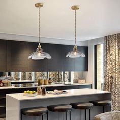 a kitchen with an island, bar stools and two pendant lights hanging from the ceiling