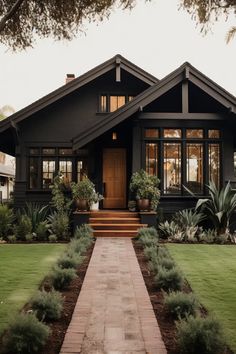 a black house with lots of windows and plants in the front yard, on a sunny day