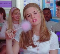 a young woman blowing on a dandelion with other people in the background