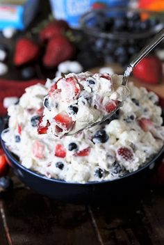 a bowl filled with fruit salad on top of a wooden table next to berries and yogurt