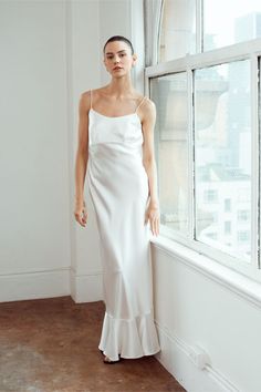 a woman standing in front of a window wearing a white dress