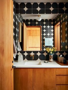 a bathroom with black and white tiles on the walls, wooden cabinets and sink area