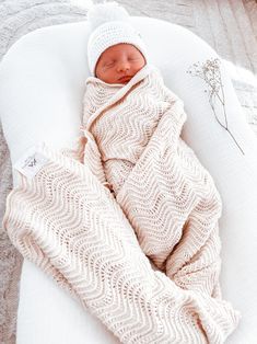 a newborn baby wrapped in a blanket on top of a white blanket and wearing a knitted hat