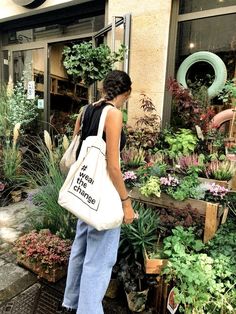 a woman carrying a tote bag in front of a flower shop filled with plants