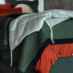 an unmade bed with green and orange bedspread on it's side