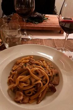 a white plate topped with pasta and mushrooms next to wine glasses on a wooden table