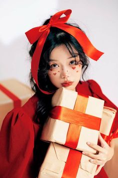 a young woman holding a wrapped present in front of her face and wearing a red dress