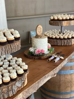 a table topped with lots of cupcakes on top of wooden trays next to wine barrels