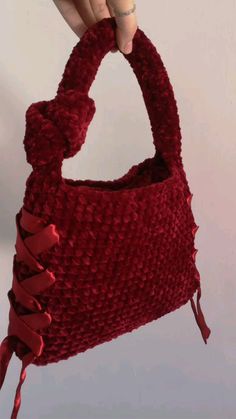 a hand is holding a red purse that has been crocheted and tied together