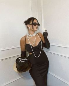 a woman in a black dress holding a hat and wearing pearls on her necklaces