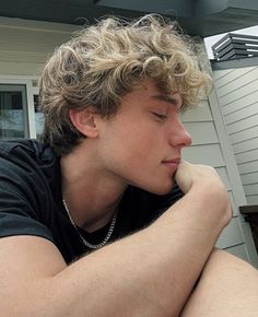 a young man sitting outside with his hand on his chin