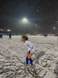 a girl is playing soccer in the snow on a snowy field at night with people watching