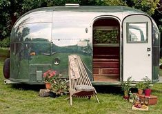 an old airstream is sitting in the grass with potted plants and other items