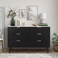 a living room with white walls and black dresser in the corner, plants on top of it