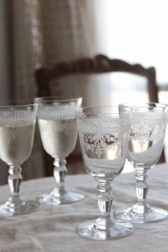 three wine glasses sitting on top of a white table cloth next to a wooden chair