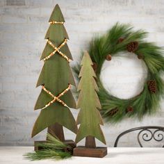 two wooden christmas trees sitting on top of a table next to a wreath and pine cones