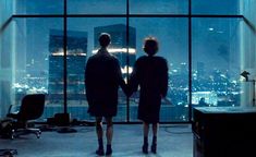 two people standing in an office looking out the window at city lights and skyscrapers