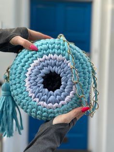 a woman holding a blue crocheted purse with a tasseled handle and chain around it