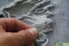 someone using scissors to cut the fabric off of a pair of denim jeans with fraying