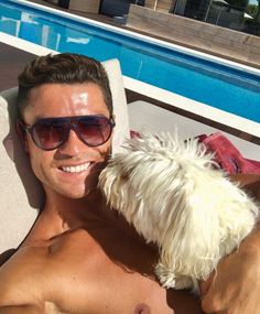 a shirtless man laying in a chair next to a white dog with sunglasses on