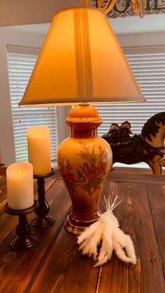 a lamp sitting on top of a wooden table next to two candles and a vase