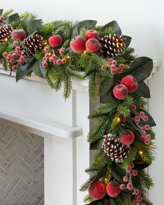 a christmas garland with pine cones and berries hanging from it's side on a fireplace mantel