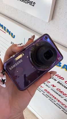 a woman holding up a purple camera in her right hand and showing it to the camera